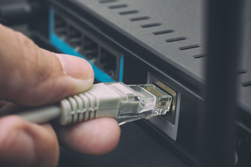 Person plugging in cable to wireless router - obrazy, fototapety, plakaty