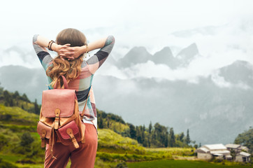 Hipster traveler with backpack enjoying view at mountains in fog.