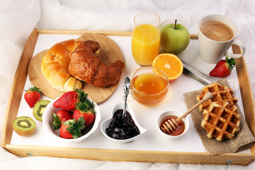 breakfast in bed with fruits and pastries on a tray -waffles, croissants, coffe and juice