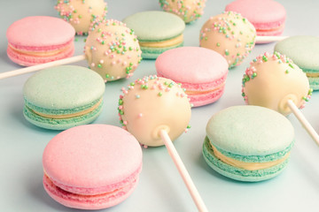 Close-up of macaroons mixed with cake pops with icing on sticks on blue background
