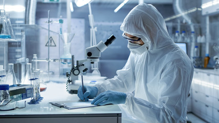 In a Secure High Level Laboratory Scientists in a Coverall Conducting a Research. Chemist Adjusts...