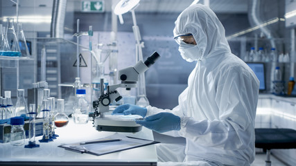 In a Secure High Level Laboratory Scientists in a Coverall Conducting a Research. Chemist Adjusts...