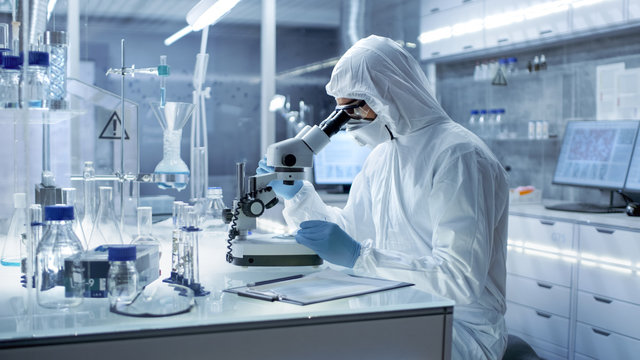 In a Secure High Level Laboratory Scientists in a Coverall Conducting a Research. Chemist Adjusts Samples in a  Petri Dish with Pincers.