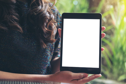 Mockup image of a business woman holding and showing black tablet with blank white screen with green nature background