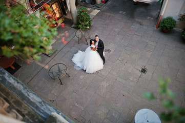 Amazing young attractive newly married couple walking and posing in the downtown with beautiful architecture and flowers on the background on their wedding day.