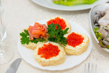 Sandwiches with red caviar and salmon are spread on a plate on a buffet table close up.