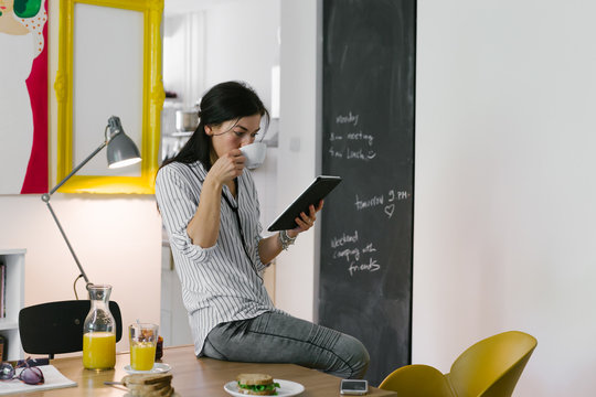 Online leisure time.young woman having breakfast while working on her tablet at home
