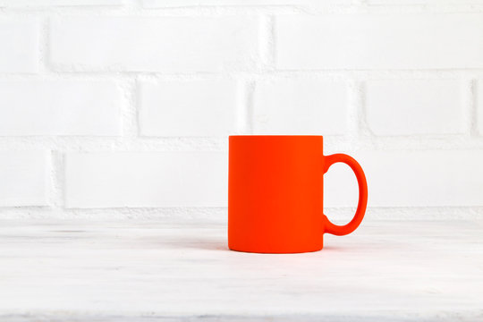 Orange mug on white table against white brick wall background. Closeup. Copy space.