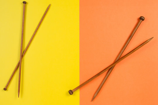 Brown wooden knitting needles on yellow and orange background
