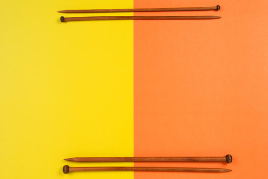 Brown wooden knitting needles arranged as frame border on yellow and orange background