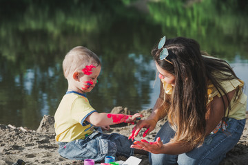 Naklejka premium Mother with the child play paints. The child plays paints on the sands.