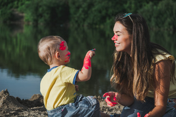 Mother with the child play paints. The child plays paints on the sands.