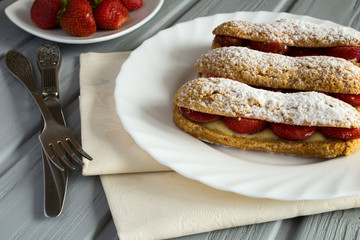 Eclairs with strawberry on the grey wooden background