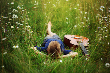Obraz premium Teenage boy lying on grass with his acoustic guitar