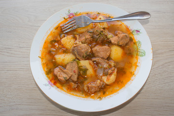 Tasty winter stew with meat and vegetables in bowl with ingredients over wooden table