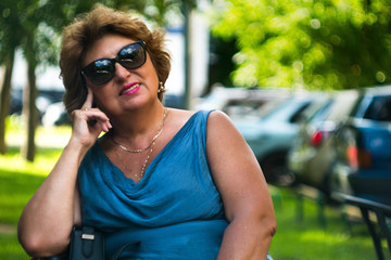 A joyful retired female. A smiling mature woman in black glasses sitting in the yard and looking at the camera