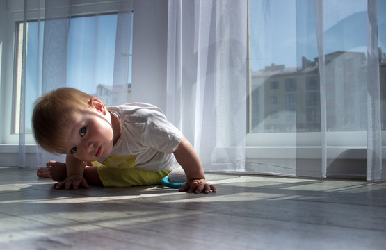 Infant child baby toddler kid sitting on wood floor and looking down on a white wall background