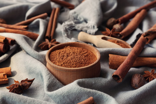 Wooden bowl with powdered cinnamon, sticks and anise on tablecloth
