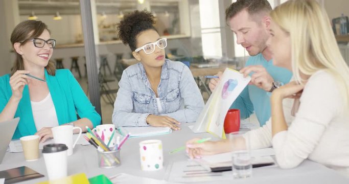 Casual man sitting with female coworkers at table and showing them folder with documents while discussing important issue.
