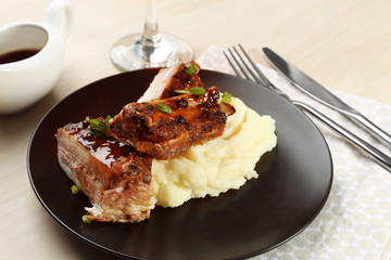 Plate with delicious pork ribs and mashed potatoes on table