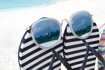 Striped flip-flops and sunglasses on sea shore, closeup. Summer vacation concept