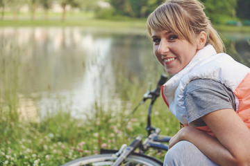 Obraz premium Young female biker next to her bike near the lake and looking in the camera.