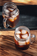 Mason jars with cold brew coffee and ice on wooden table
