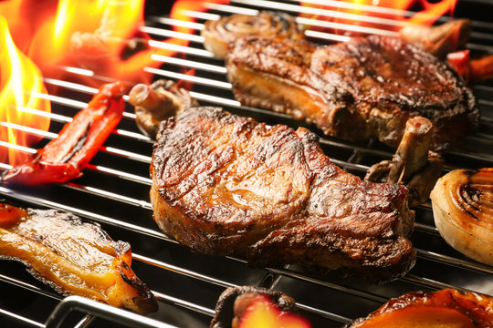 Delicious steak with vegetables on grilling grid and flame, closeup