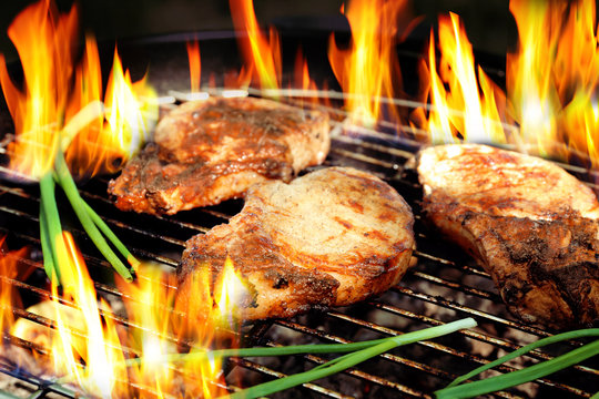 Delicious steaks on grilling grid and flame, closeup