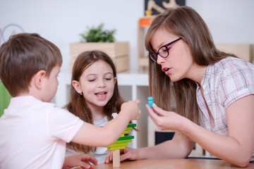 Obraz na płótnie Canvas Preschool Teacher and Kids Playing with Wooden Toy Building Blocks