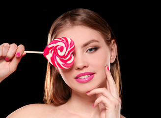 Beautiful young woman with lollipop on black background