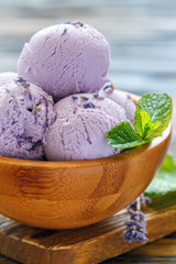 Lavender ice cream and mint leaves in a wooden bowl.