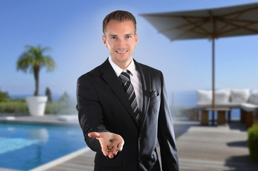 Agent immobilier présentant une clef dans sa main devant une magnifique piscine 