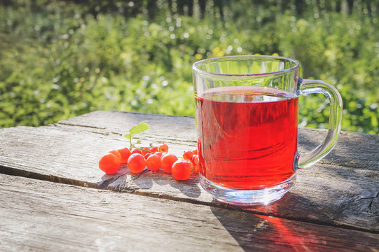 A glass beaker with berry compote stands on an old wooden table in the garden.