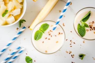 Summer fruits, refreshing drinks. Vegan food. Breakfast. Smoothie of yogurt, raw organic yellow melon, flax seeds and mint. With striped straws, in glasses, white marble table, copy space top view
