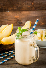 Summer fruits, refreshing drinks. Vegan food. Breakfast. Smoothie of yogurt, raw organic yellow melon, flax seeds and mint. With striped straws, in mason jar, wooden rustic table, copy space
