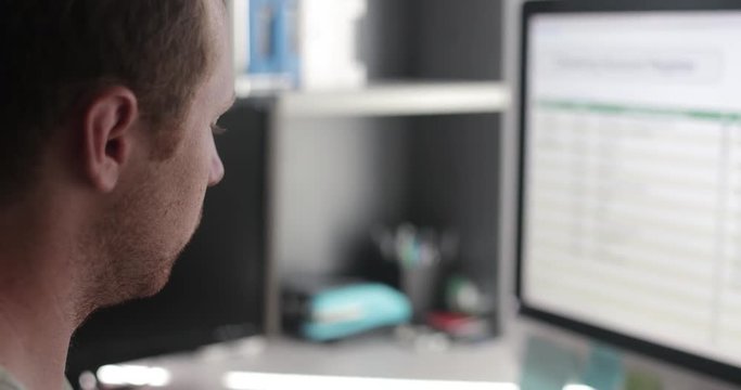 Freelancing man works in his home office on a desktop computer for remote work.