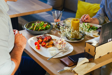 At the table, two men eat dinner, eat a steak, with a salad on a white plate, with a fork and knife in their hands.