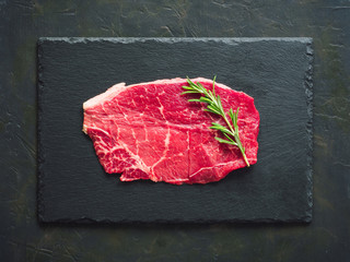 Close-up of raw fresh black angus beef with fresh rosemary. Top view of beef schnitzel on dark...