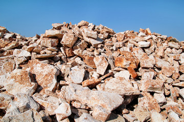 Brown Granite. Big pile of rocks for construction and boulders piled in a heap under a blue sky in summer time. A large pile of limestone in quarry. Pile of gravel and construction material.