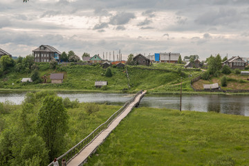north Russian village Isady. Summer day, Emca river, old cottages on the shore, old wooden bridge and clouds reflections.