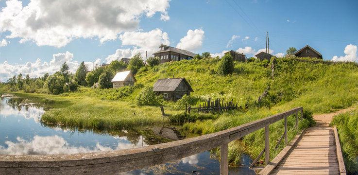 north Russian village Isady. Summer day, Emca river, old cottages on the shore, old wooden bridge and clouds reflections.