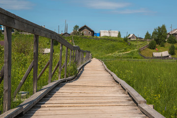 Fototapeta na wymiar north Russian village Isady. Summer day, Emca river, old cottages on the shore, old wooden bridge and clouds reflections.