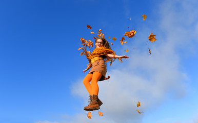 A young child feels joyful about autumn arriving. She throws colored leaves in  the air and expresses her Autumn happiness. 
