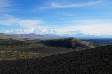 View over a black volcanic lava landscape from the Inferno Cone. A cinder cone rising above a landscape of black volcanic basalt rock and volcano domes from eruptions. Craters of the Moon.