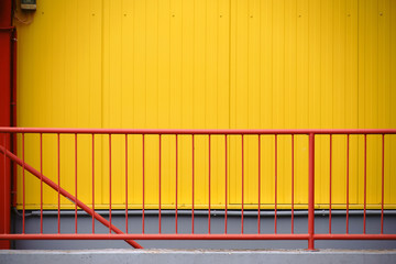 Geländer vor gelber Wand  / Ein farbenfrohes rotes Geländer vor der gelben Riffelblechfassade...