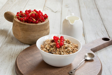 Summer healthy breakfast of muesli with milk jug with red currant decor on wooden board.