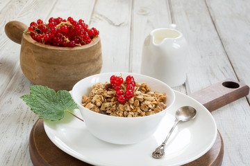 Summer healthy breakfast of muesli with milk jug with red currant decor on wooden board.