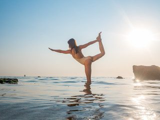 Fototapeta na wymiar Young caucasian woman in swimsuit practicing yoga in water sea or oceanr. Beautiful reflection. Complex asanas, balance. Fitness, sport, yoga and healthy lifestyle concept.