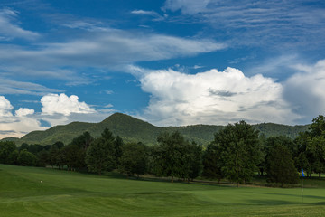 A Summer Storm rises over a mountain ridge behind the fairway and green of a golf course